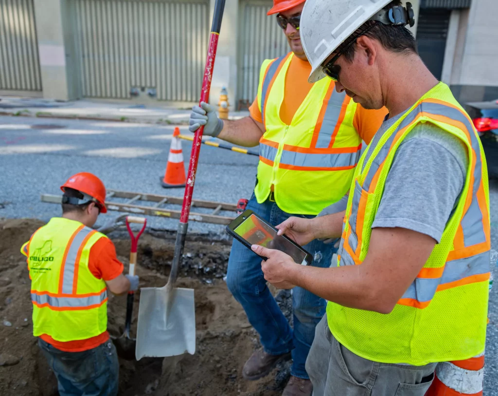 Workers digging hole, consulting tablet