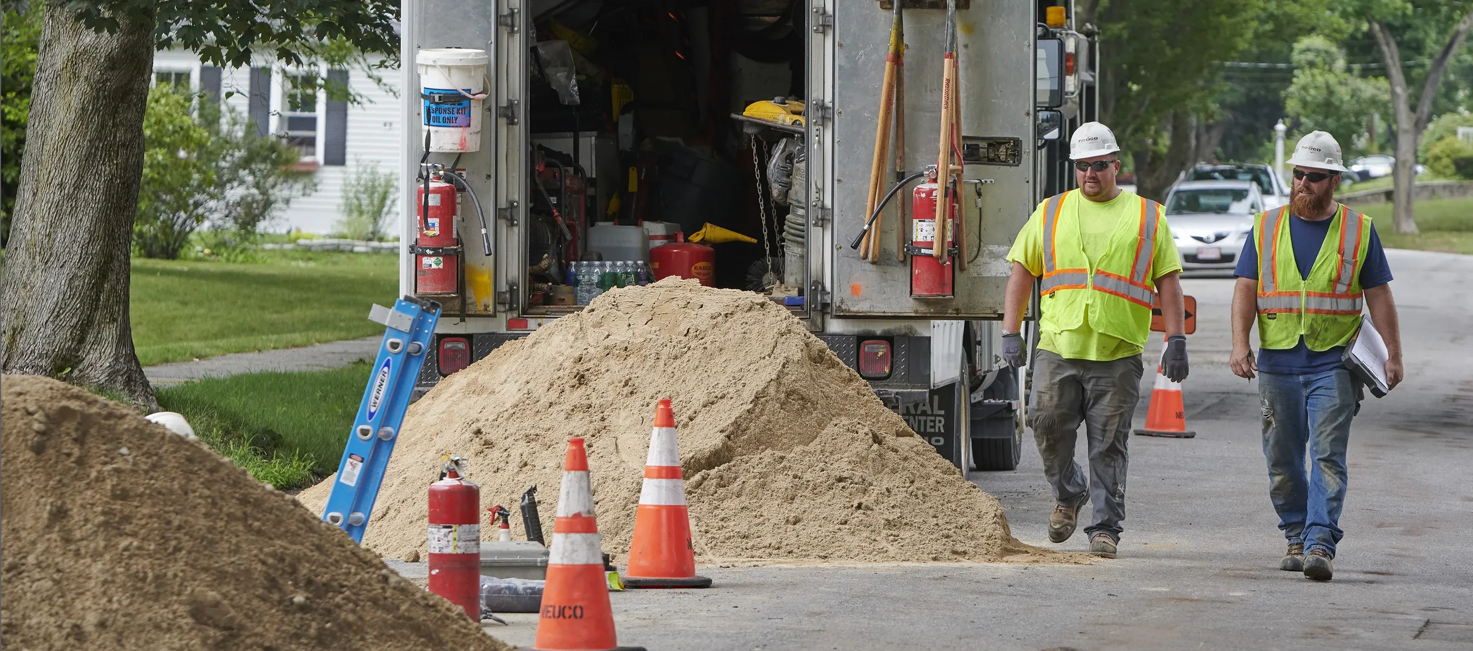 Two workers in hard hats and safety glasses walk through job site